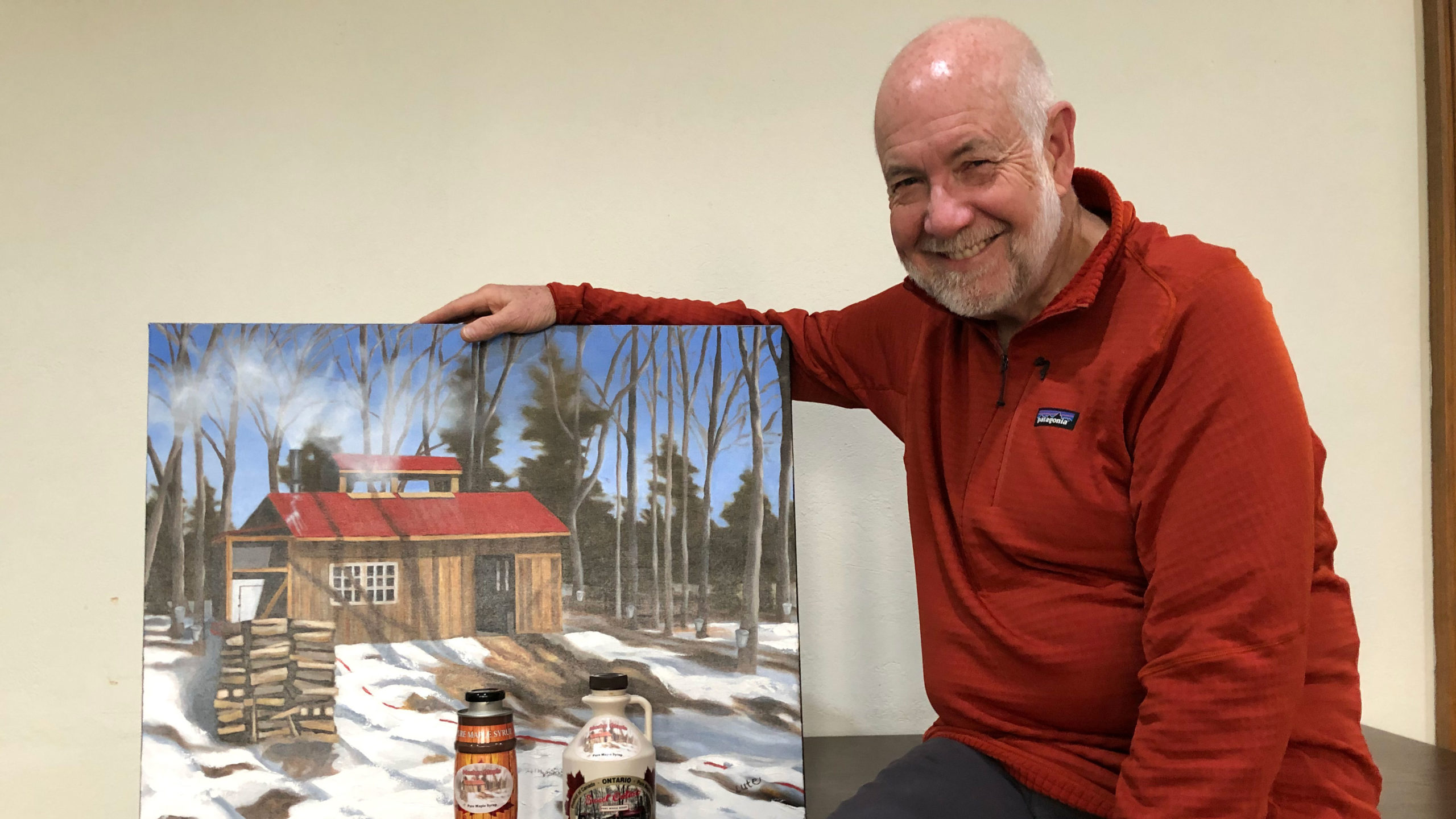 Larry with his maple syrup and a painting of the Sugar Shack by Graham Lute.