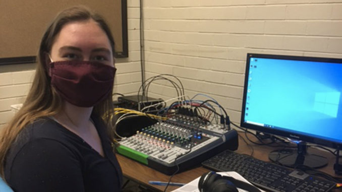 Sydney Murray is a teen sitting at a computer with a mask on. Photo by Sherri Golisky.